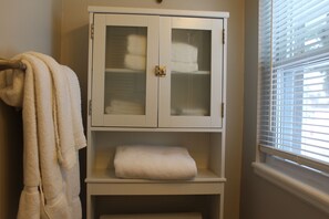 Een badkamer met een witte kast met handdoeken, een handdoekhouder en een raam met jaloezieën.