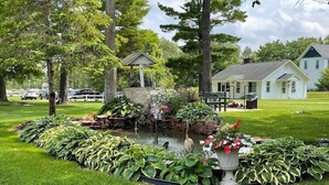 A well-maintained garden with a pond, surrounded by lush greenery and a gazebo. - Cozy Riverfront Getaway | 1BR + Sleeper Sofa (Indian River)