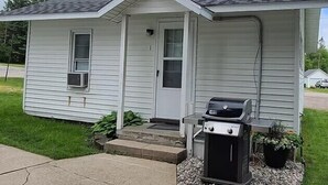 A single-story house with a front porch, a door, and a small attached garage with a grill. - Cozy Riverfront Getaway | 1BR + Sleeper Sofa (Indian River)