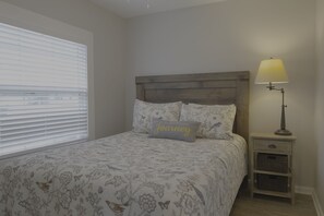Um quarto com cama, mesa de cabeceira, luminária e janela com persianas.