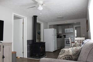 A living room with a fireplace, a sofa, and a television. There is a kitchen area with cabinets and a microwave.