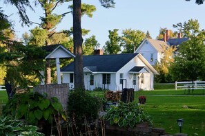 A white house with a dark roof, surrounded by greenery and a white fence.