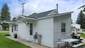 A small, single-story house with a covered patio area featuring a picnic table and grill. - Charming 2BR Cabin | River Views & Outdoor Space (Indian River)