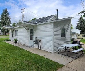 A small, single-story house with a covered patio area featuring a picnic table and grill.