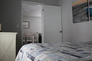 A bedroom with a bed, a door, a chair, a desk, and a framed picture on the wall.