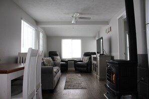 Un salon avec une cheminée, un ventilateur de plafond et un téléviseur posé sur un meuble.