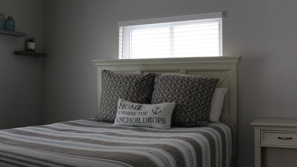 A bedroom with a bed, pillows, a nightstand, a window, and shelves with decorative items. - Charming 2BR Cabin | River Views & Outdoor Space (Indian River)