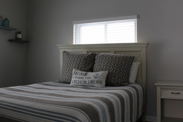 A bedroom with a bed, pillows, a nightstand, a window, and shelves with decorative items.