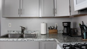 A kitchen with a granite countertop, stainless steel sink, and a gas stove. - Charming 2BR Cabin | River Views & Outdoor Space (Indian River)