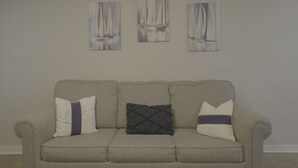 A neutral-toned sofa with three cushions against a plain wall, with three paintings of sailboats above. - 1BR Hideaway | Steps from Indian River (Indian River)