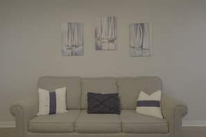 A neutral-toned sofa with three cushions against a plain wall, with three paintings of sailboats above. - 1BR Hideaway | Steps from Indian River (Indian River)