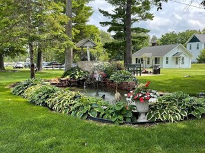 A well-maintained garden with a pond, surrounded by lush greenery and a gazebo.
