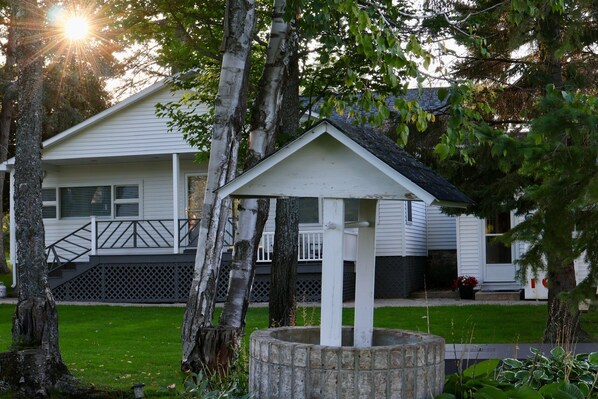 A white building with a porch, surrounded by trees and a well-maintained lawn.