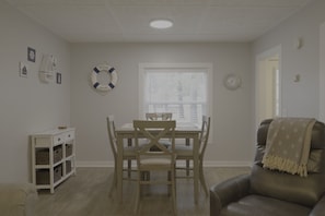A dining area with a wooden table and chairs, a white cabinet with baskets, a life preserver decoration, and a clock on the wall.