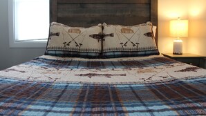 Una cama con una colcha escocesa y dos almohadones decorativos con motivos de pesca.