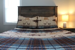 Una cama con una colcha escocesa y dos almohadones decorativos con motivos de pesca.