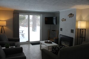 A living room with a fireplace, a flat-screen TV, and a large window.