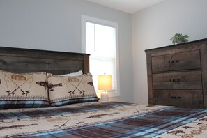 A bedroom with a bed, pillows, a bedside lamp, and a dresser.