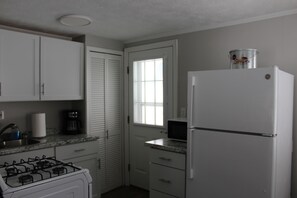 A kitchen with white cabinets, a stove, a refrigerator, and a window.