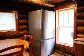 Une cuisine compacte dotée d’un réfrigérateur en acier inoxydable, de murs en bois, d’une table à manger en bois avec une chaise rouge et d’une fenêtre laissant entrer la lumière naturelle.