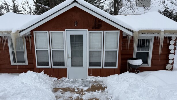 A wooden cabin with a snow-covered roof and a front door. - Rustic Riverfront Getaway (Indian River)