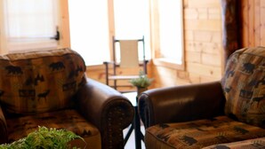 Um quarto acolhedor com um sofá e poltronas de couro, uma pequena mesa com uma planta e vista para o exterior pela janela.