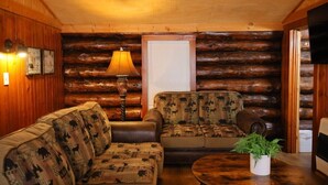 Interior acolhedor de uma cabana de madeira, com sofá, poltrona e luminária.