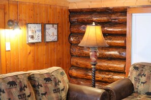 A log cabin interior with a wooden wall, a lamp, and two patterned sofas.