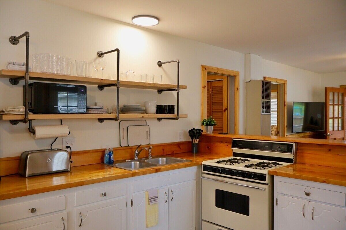 A kitchen with wooden countertops, a stove, a microwave, and shelves holding dishes and glasses.