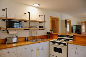 A kitchen with wooden countertops, a stove, a microwave, and shelves holding dishes and glasses.