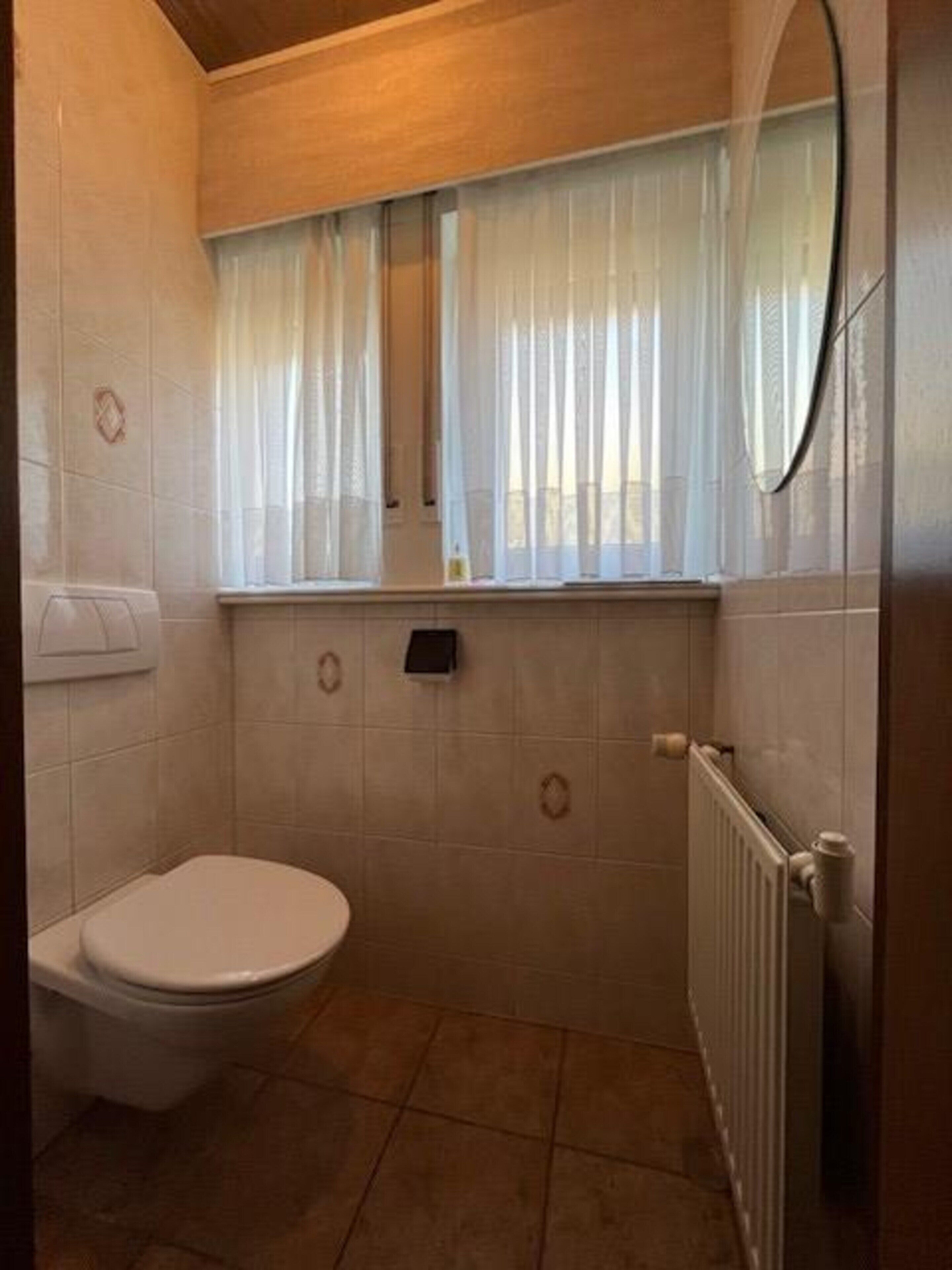 Un baño con inodoro, una ventana con cortina y un radiador.