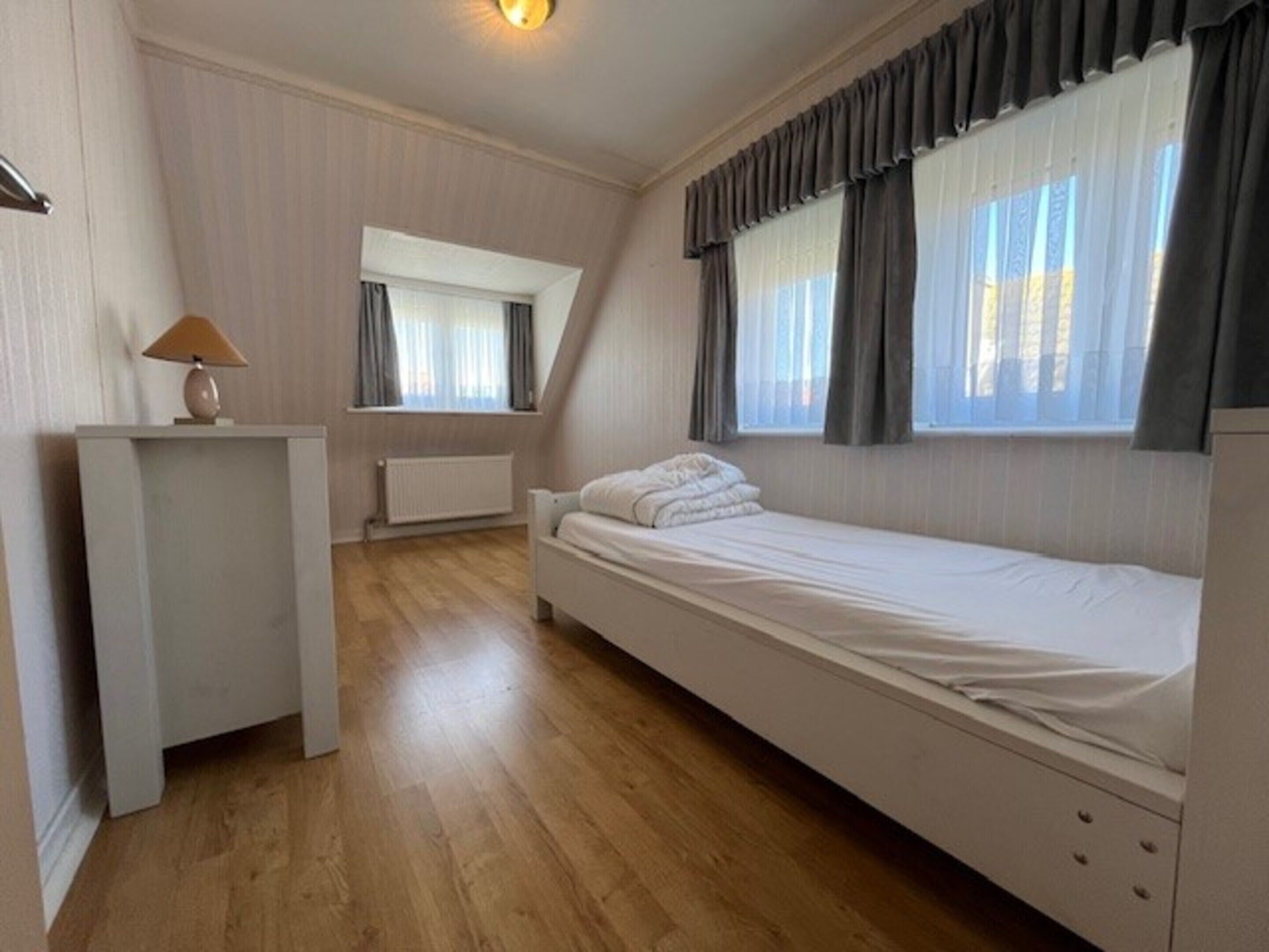 A small, tidy room with a single bed, a desk, and a window with curtains.