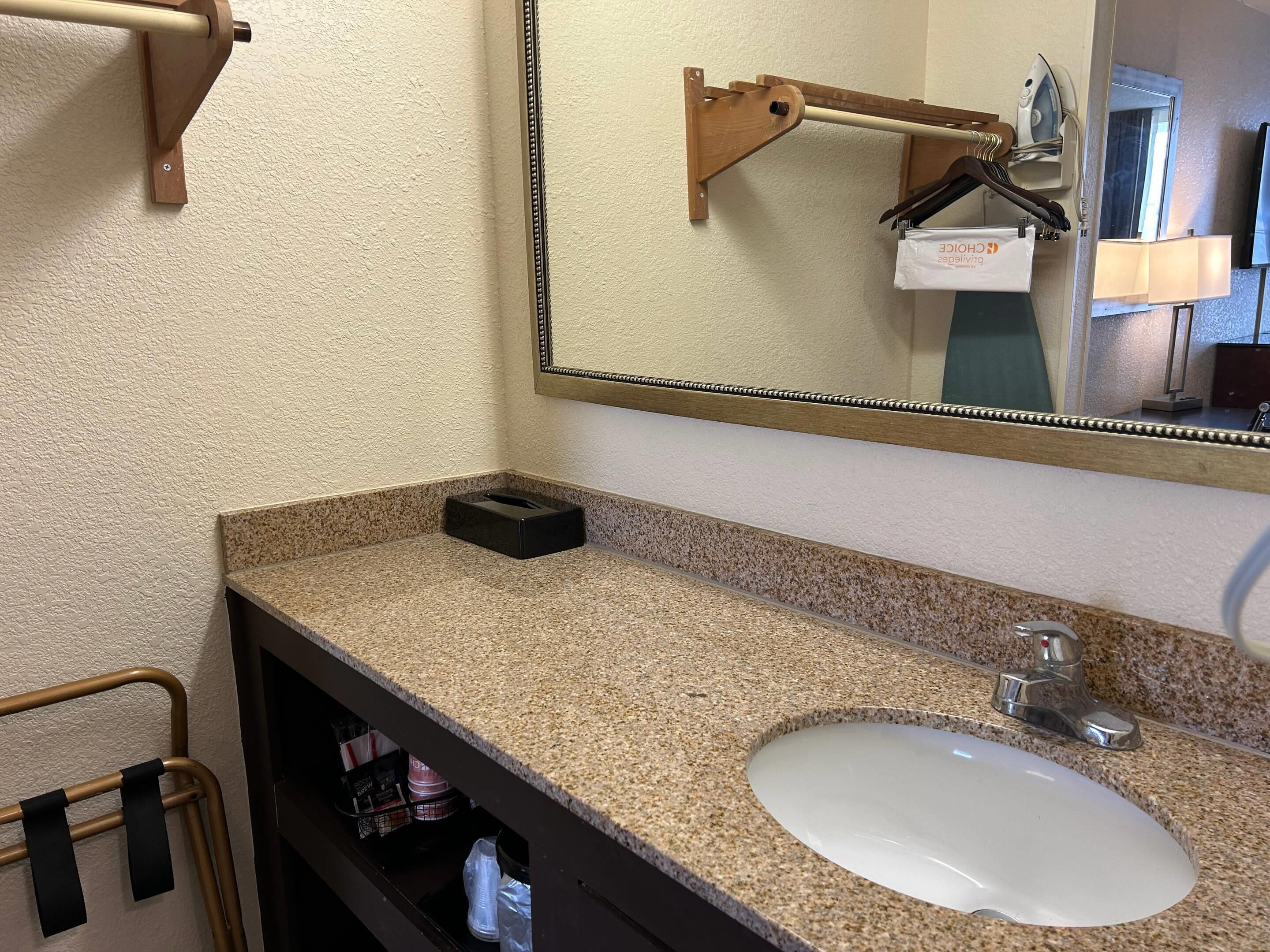A bathroom with a granite countertop, a white sink, a mirror with a wooden frame, and a towel rack.