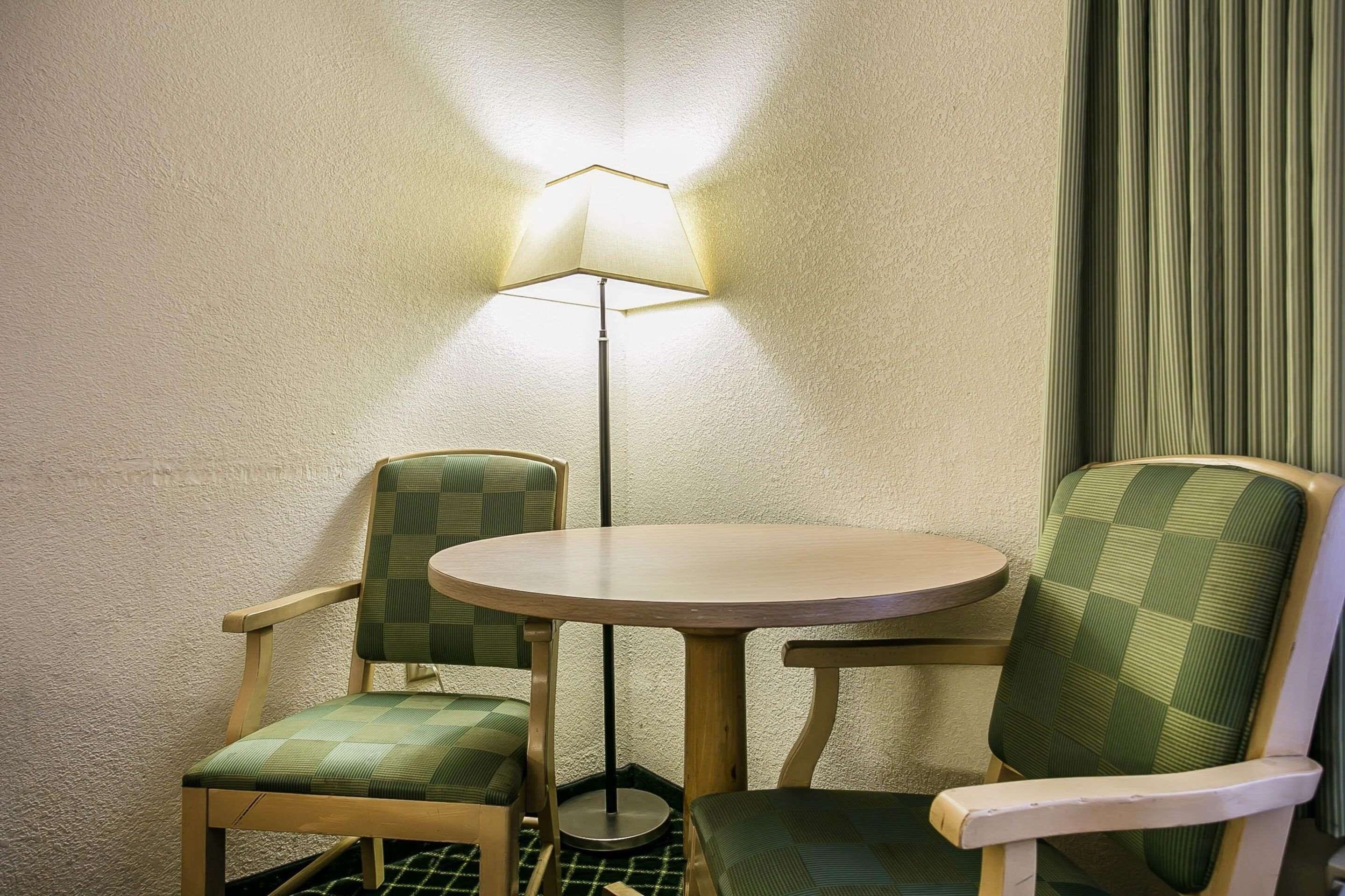 A corner room with a round table and two chairs, a floor lamp, and a curtain.