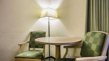 A corner room with a round table and two chairs, a floor lamp, and a curtain.