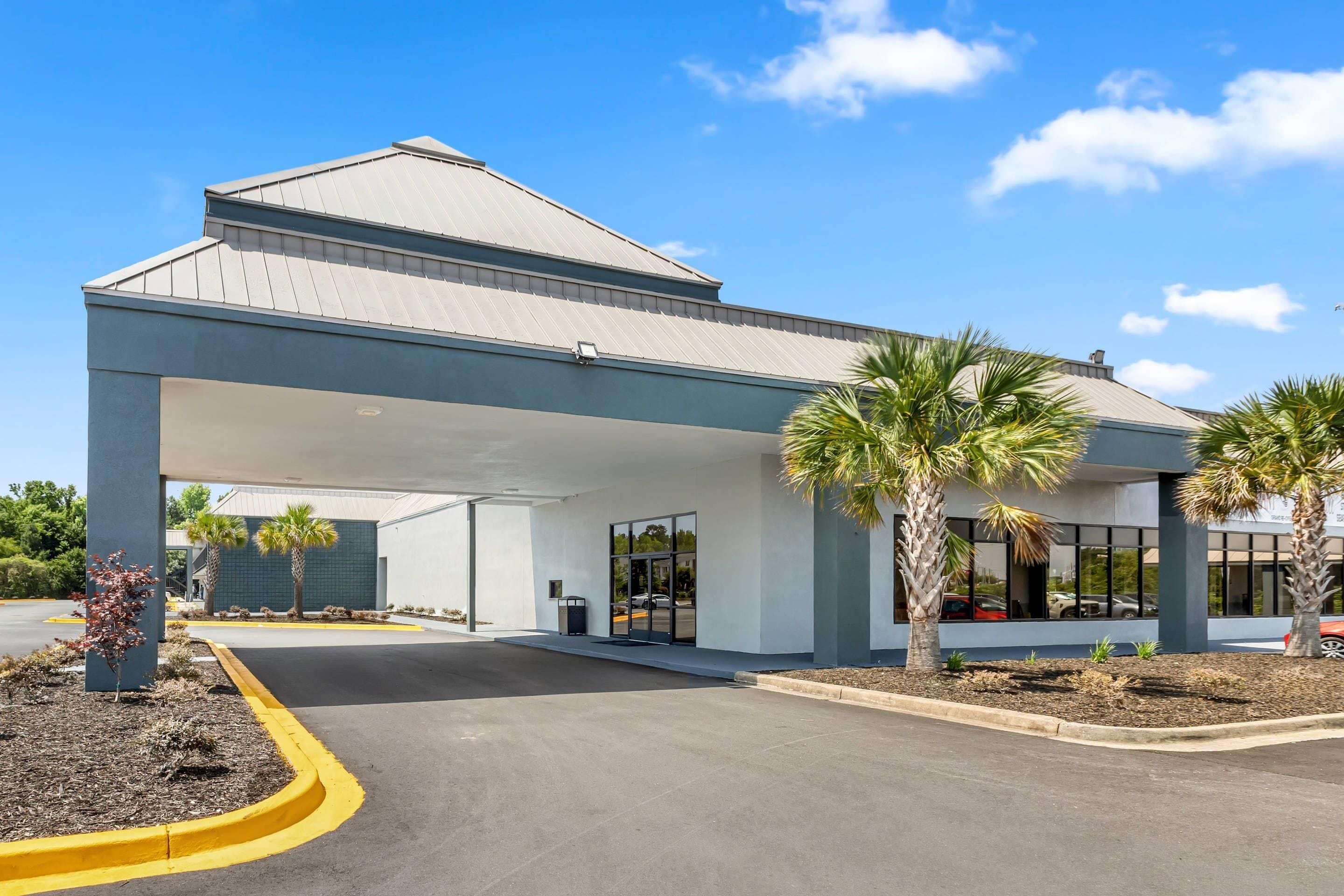 A hotel entrance with a covered walkway, palm trees, and a clear sky.