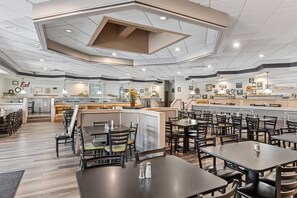 En rummelig restaurant med flere spiseområder, en bar og et køkken i baggrunden.