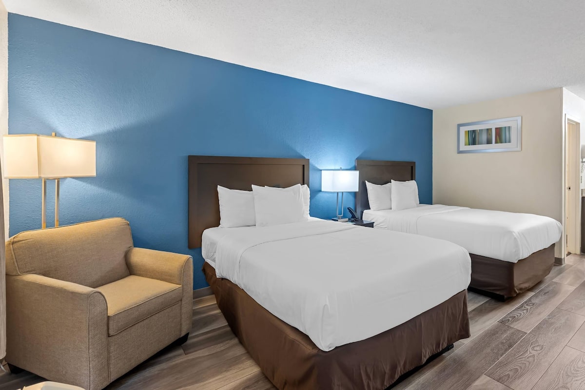Quarto de hotel com duas camas, um sofá e uma luminária.