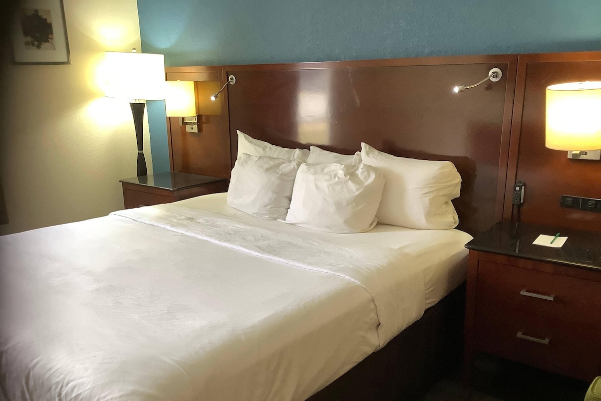 Quarto de hotel com uma cama grande, duas mesas de cabeceira e duas luminárias fixadas na parede.