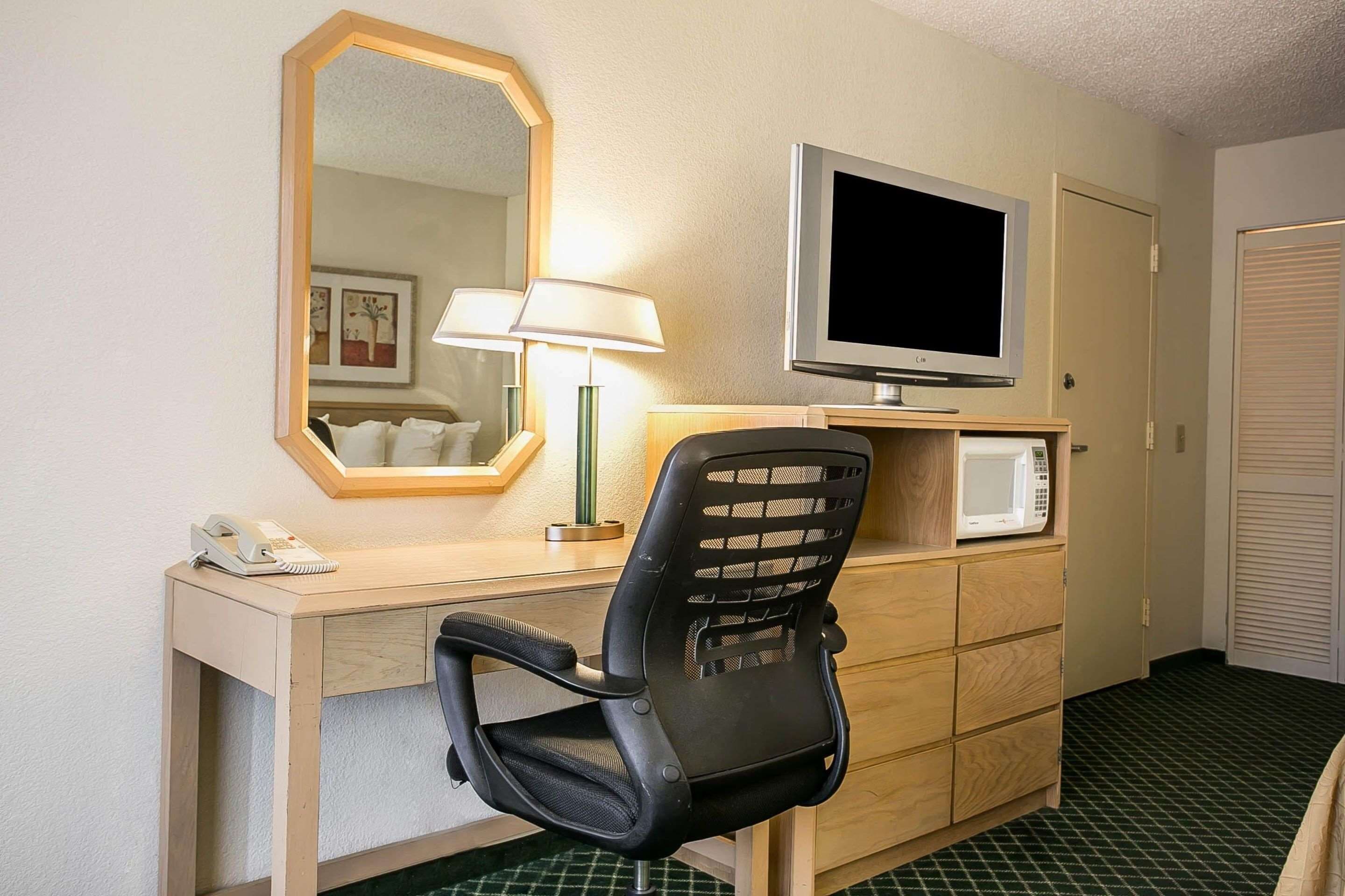 A hotel room with a desk, a chair, a television, a microwave, a telephone, and a mirror.