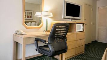 A hotel room with a desk, a chair, a television, a microwave, a telephone, and a mirror.