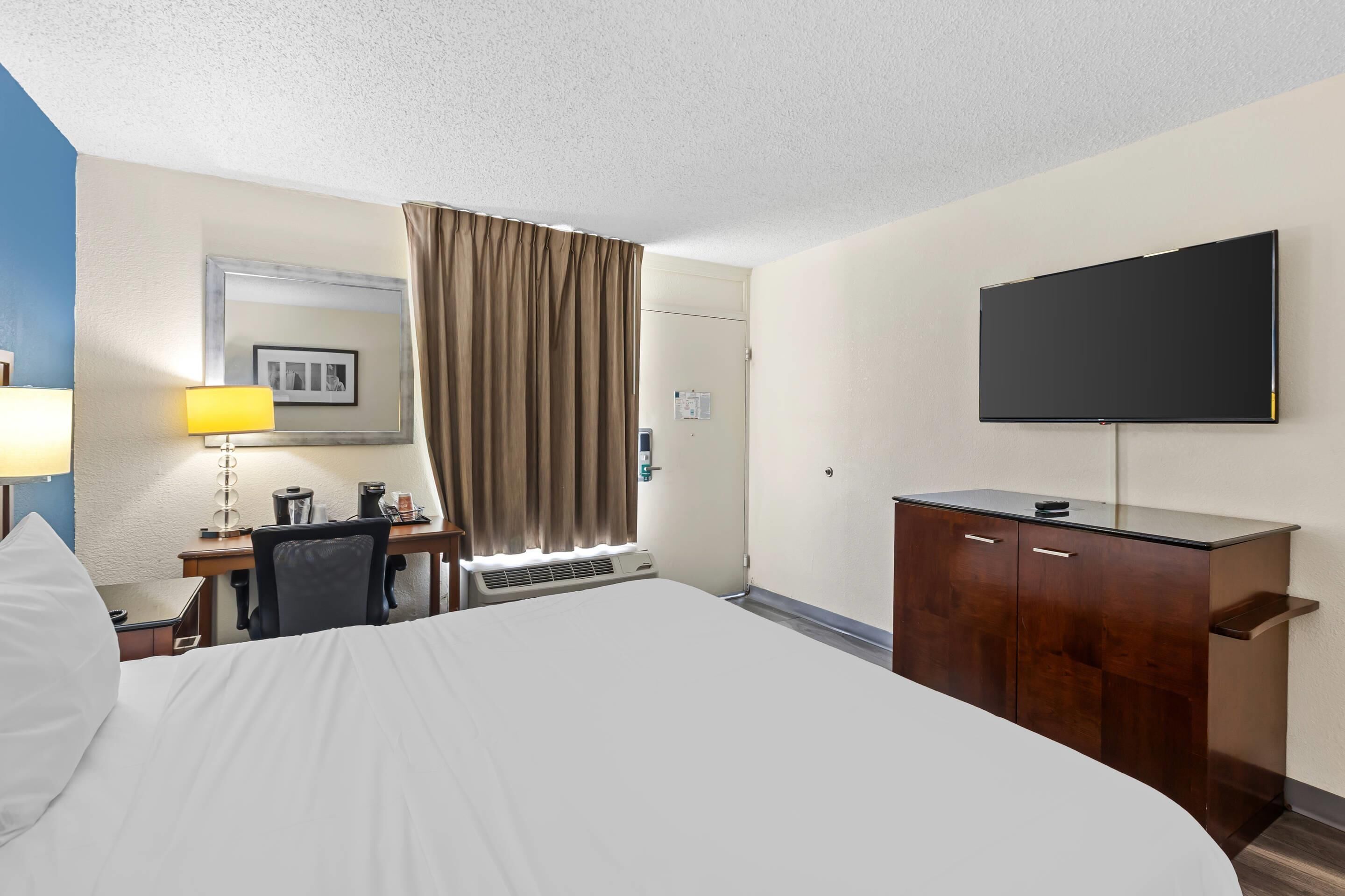 A hotel room with a bed, a desk with a lamp, a television, and a wardrobe.