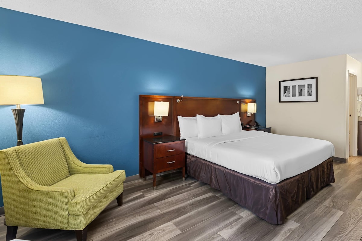 Quarto de hotel com cama, mesas de cabeceira, abajur, cadeira e um quadro na parede.