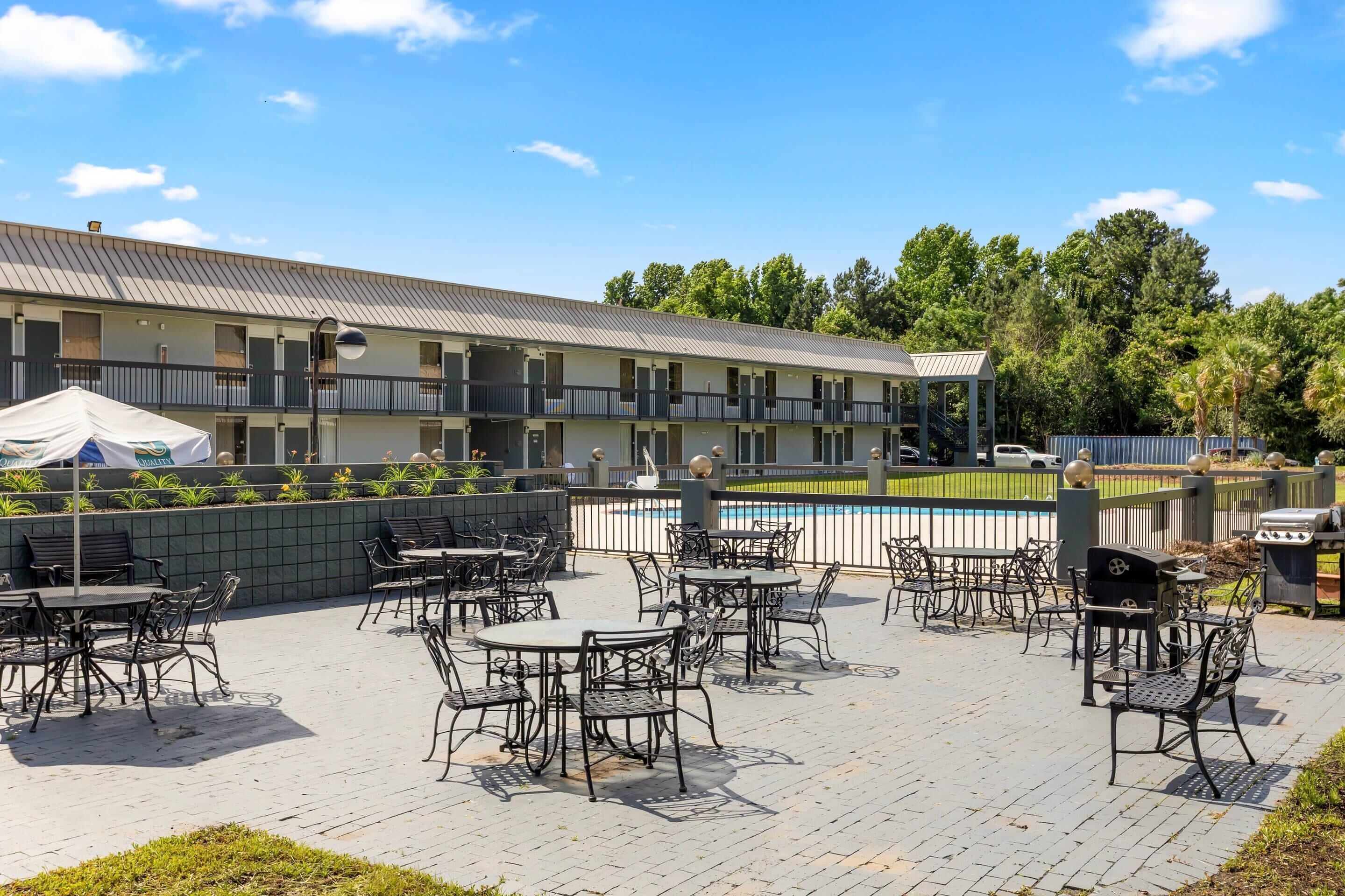 A hotel with outdoor patio seating, a pool, and a barbecue area.