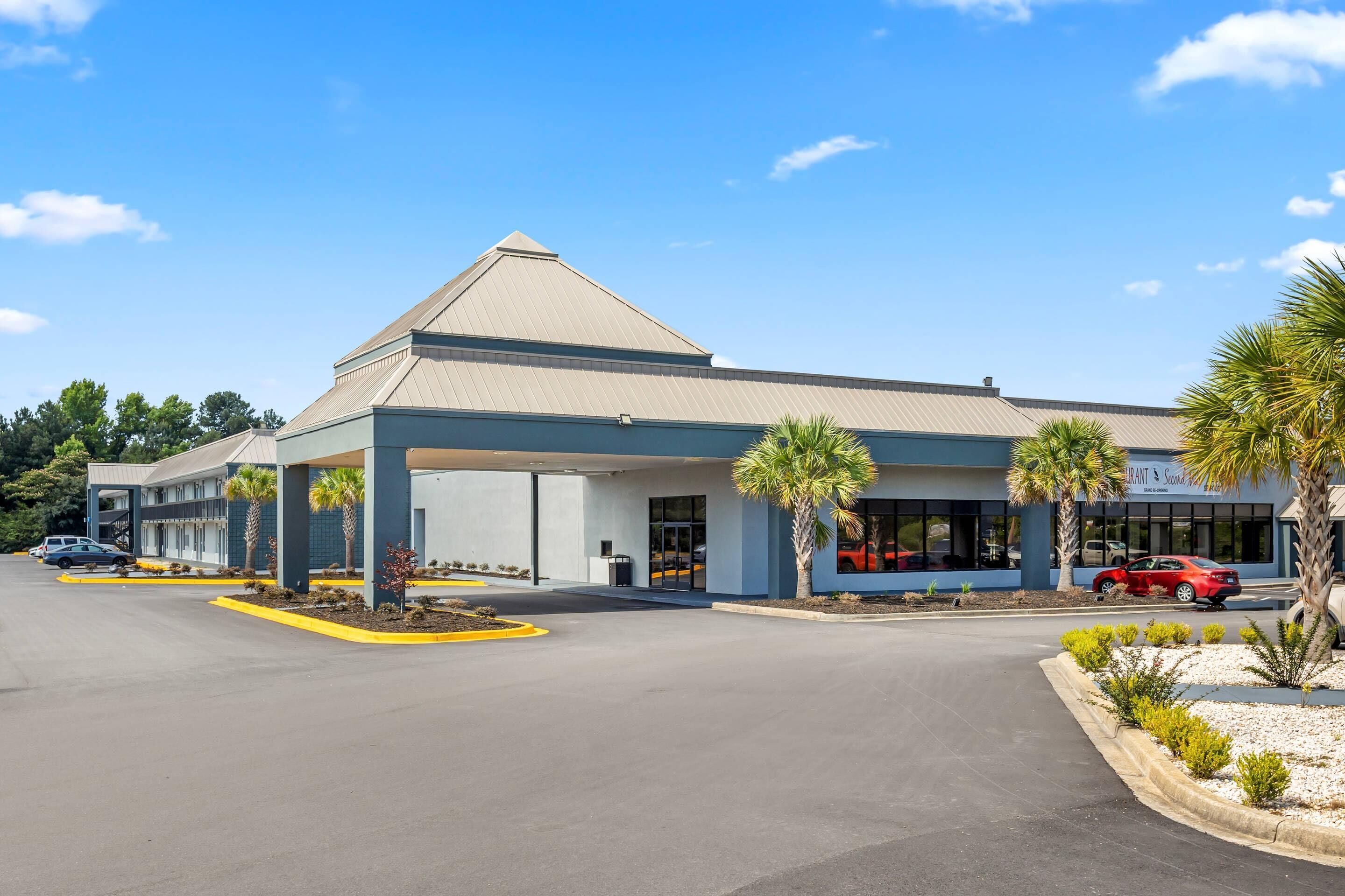 A hotel with a covered parking area, palm trees, and a red car parked outside.