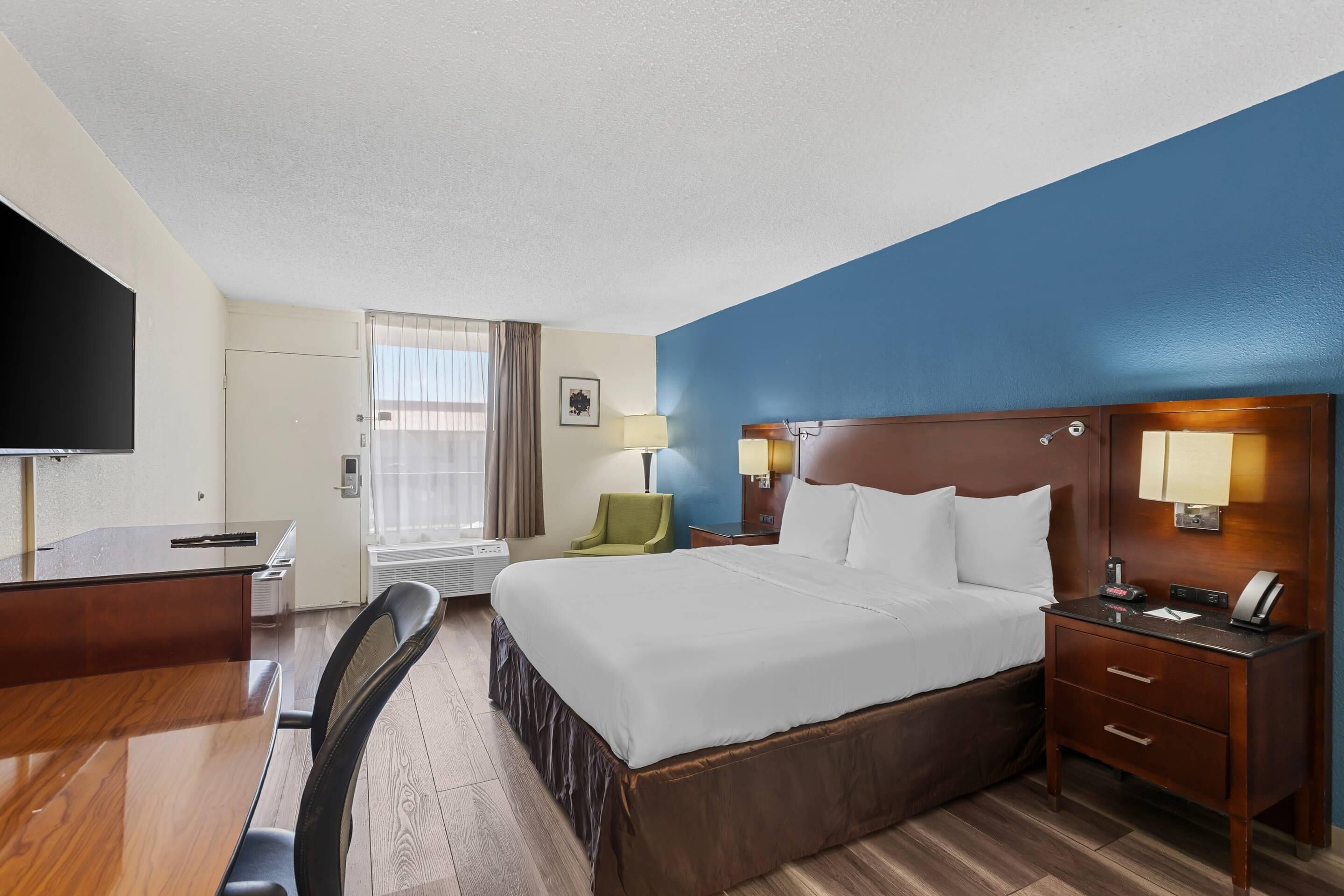 A hotel room with a bed, desk, chair, TV, and a window with curtains.