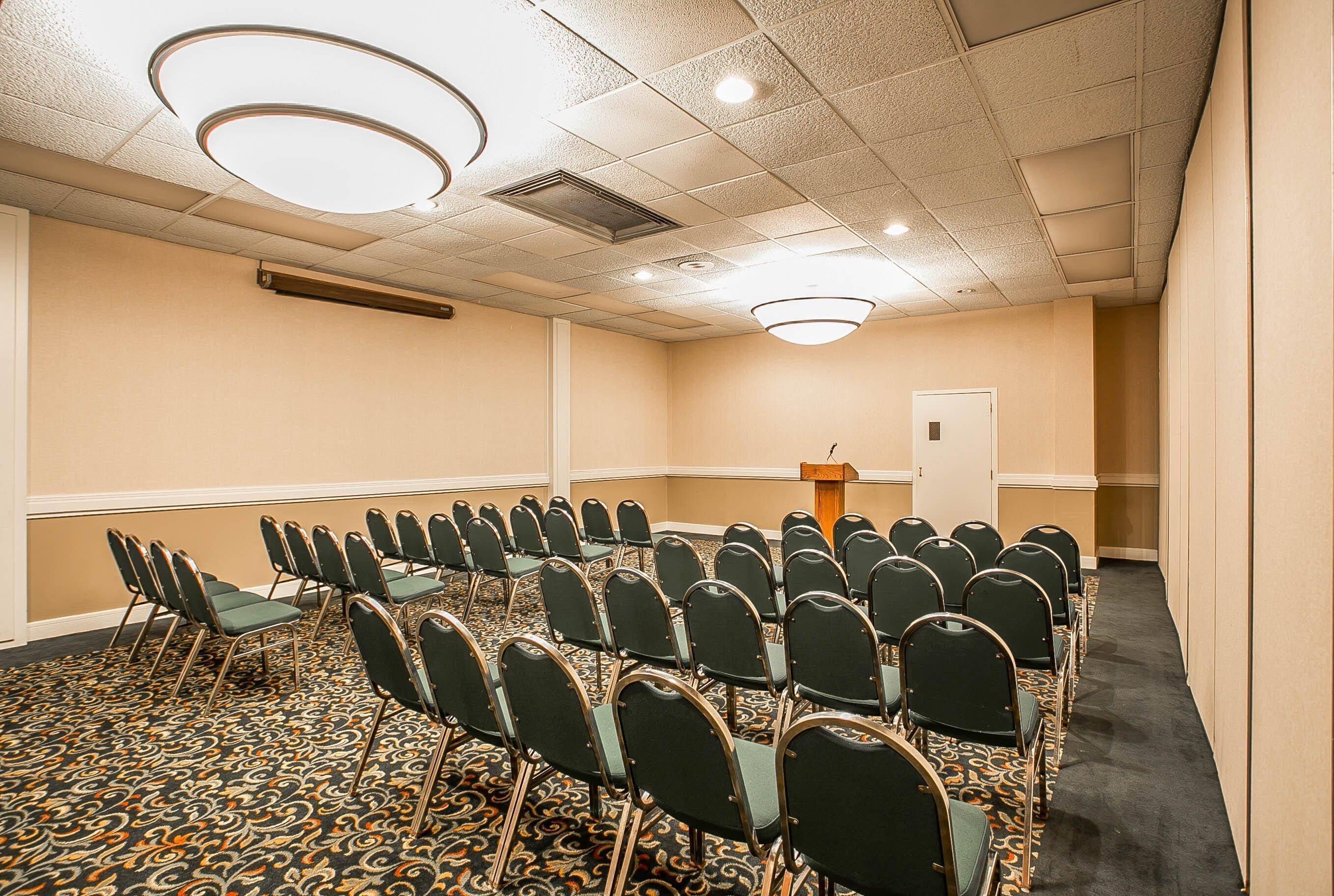 A conference room with rows of chairs, a podium, and a carpeted floor.