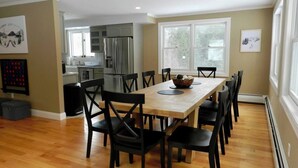 A dining area with a wooden table and black chairs, a kitchen in the background, and a large window providing natural light. - Southern Vermont Retreat w/ Hot Tub, Fire Pit, & Bunk Room (Windham)