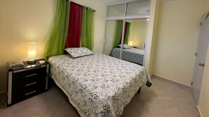 Een slaapkamer met een bed, een nachtkastje, een spiegel en een plafondventilator.