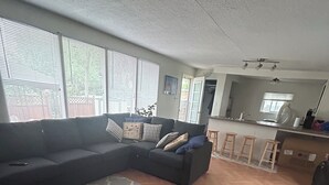 Una sala de estar con un sofá modular, un tapete estampado y una zona de cocina con barra.